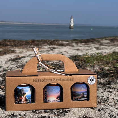 Coffret bougies artisanales Bretagne posé sur plage avec phare en arrière-plan